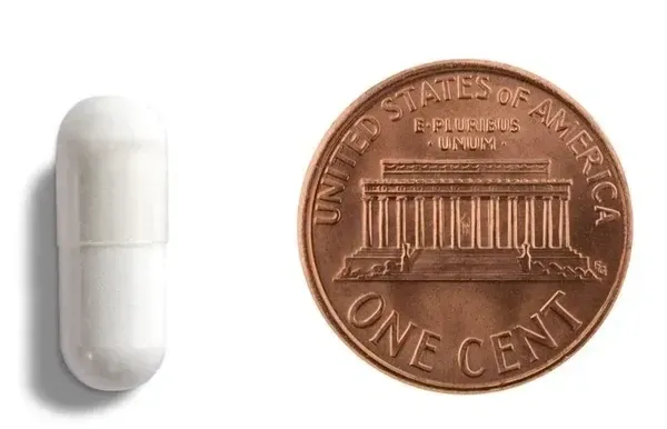 White capsule next to a penny coin.