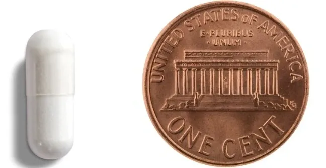 White capsule next to a penny.