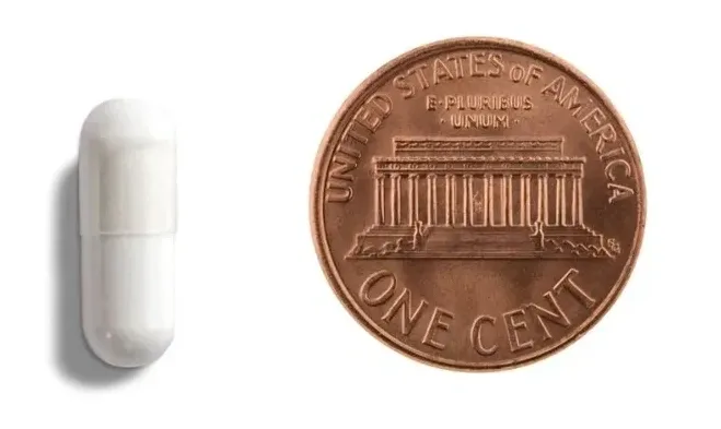 White capsule beside a U.S. penny.